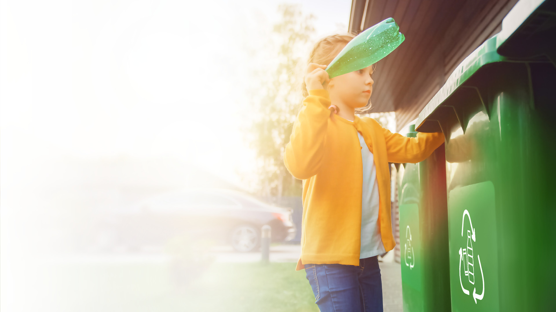 Junges Mädchen wirft eine leere Plastikflasche in einen Mülleimer. Sie benutzt den richtigen Mülleimer. Recycling