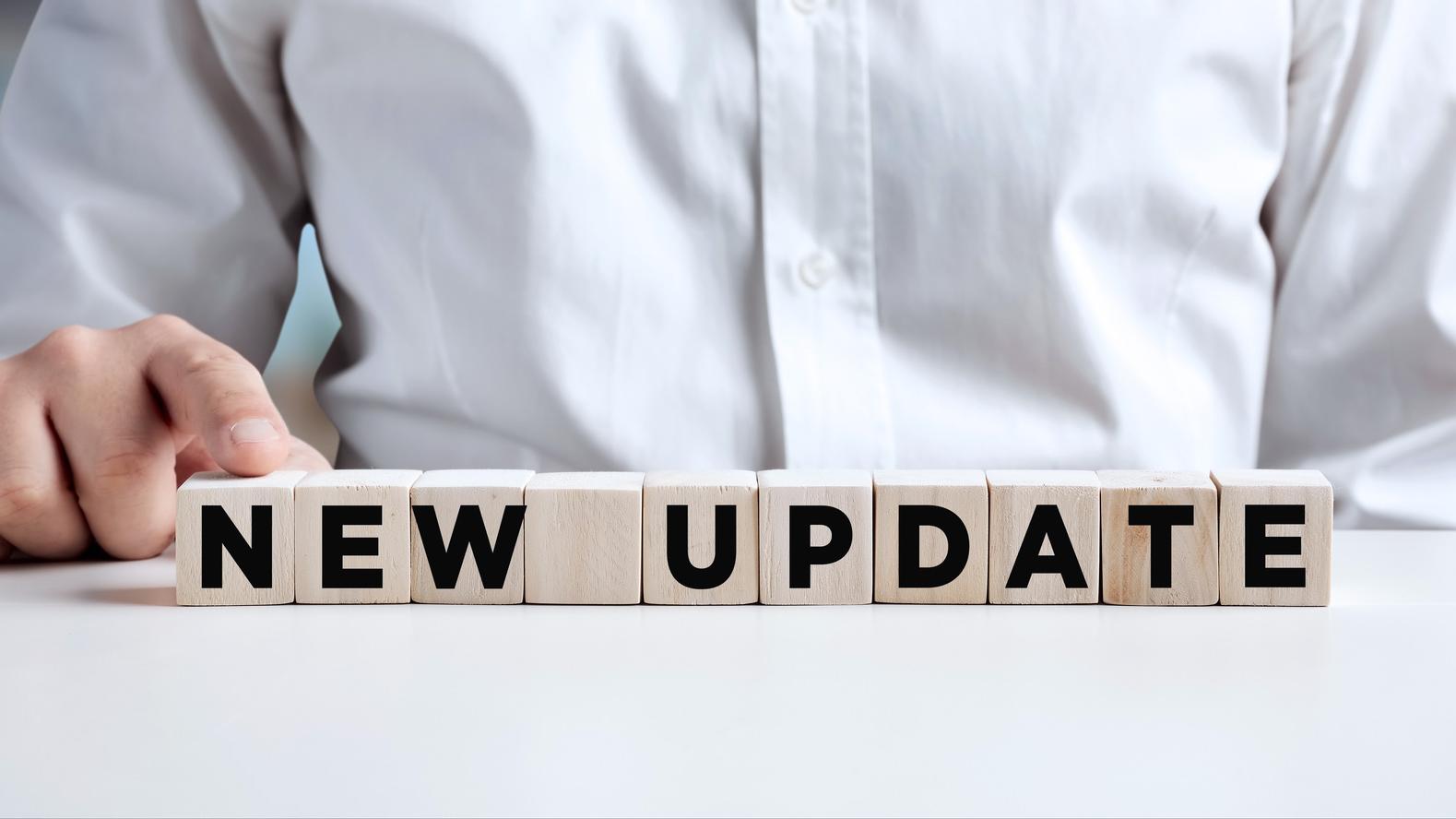 Ein Geschäftsmann drückt mit dem Finger auf einen Holzwürfel mit dem Wort "New Update"