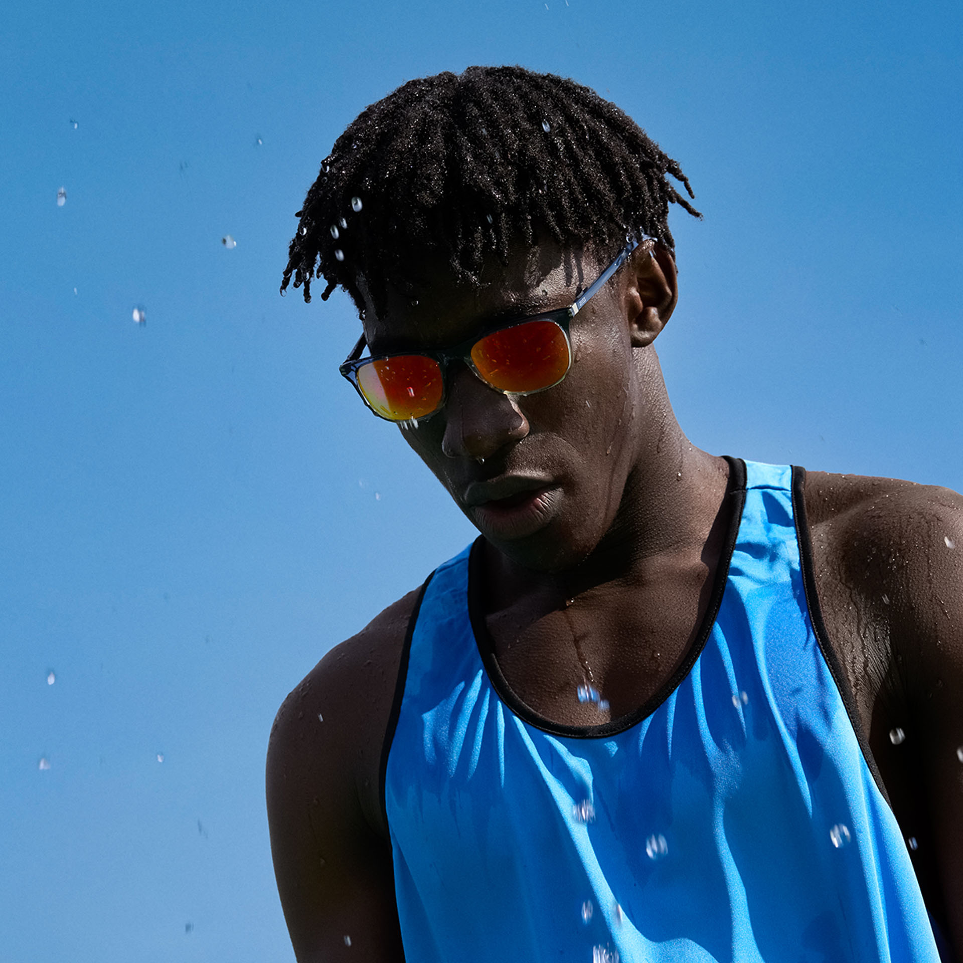 &quot;Ein junger Mann in Sportbekleidung mit ZEISS Sport Sonnenbrillengläsern in einem braun-orangen Ton vor dem blauen Himmel.&quot;