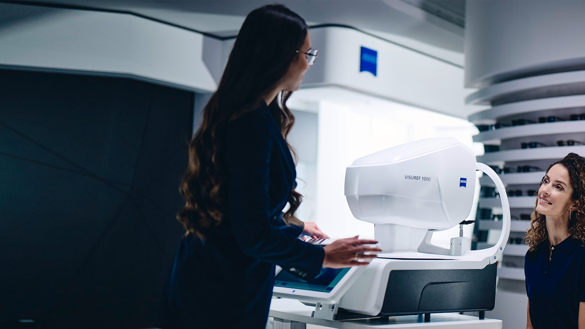 Eine Frau sitzt vor einem ZEISS VISUREF 1000 und sieht eine Optikerin an.