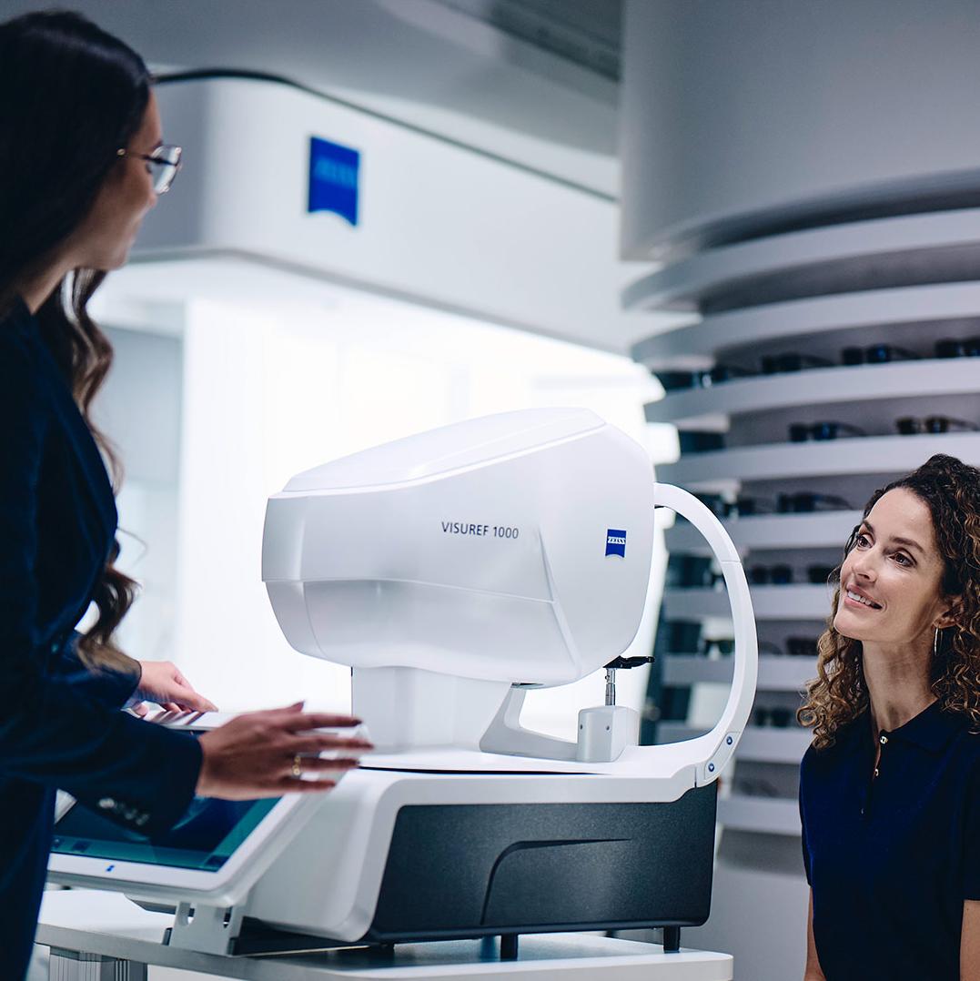 Eine Frau sitzt vor einem ZEISS VISUREF 1000 und sieht eine Optikerin an.