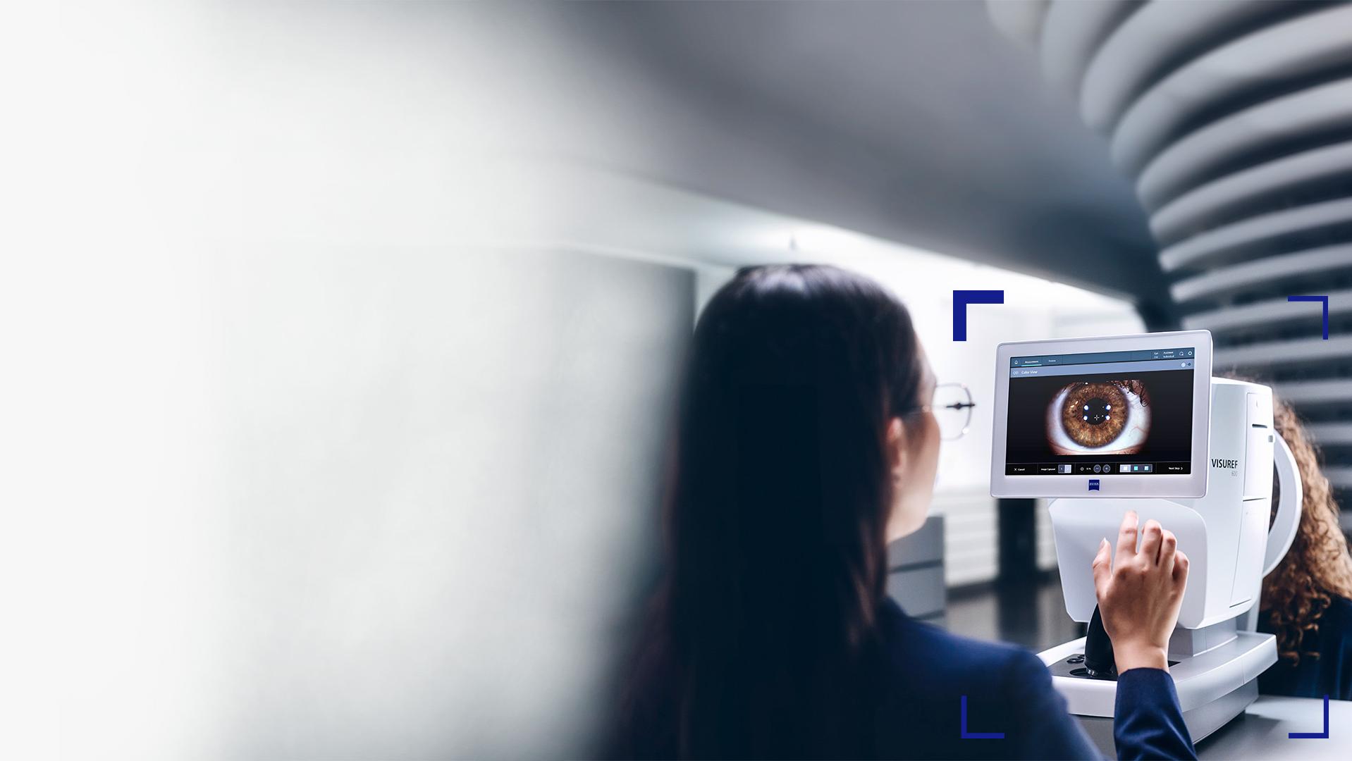 Eine Augenoptikerin schaut auf den Bildschirm eines ZEISS VISUREF 600, auf dem das Bild eines Auges zu sehen ist.