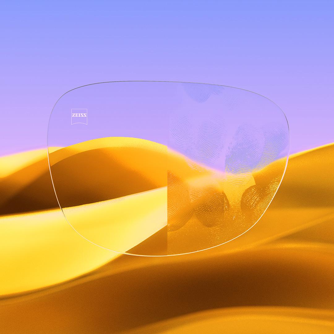 Ein Brillenglas im Vergleich: Eine Seite klar und sauber mit ZEISS DuraVision Gold UV, die andere Seite bedeckt mit Fingerabdrücken.