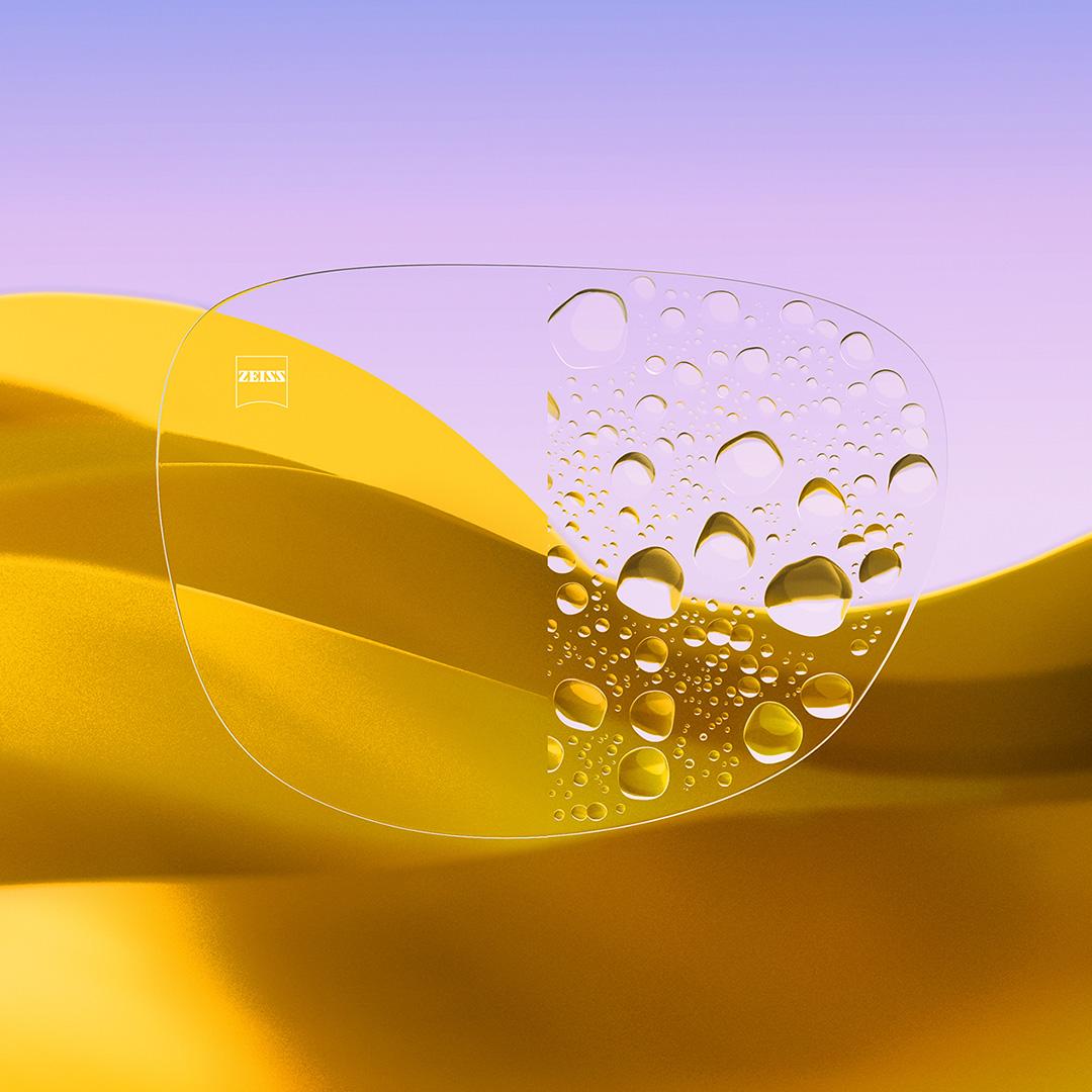 Ein Brillenglas im Vergleich: Eine Seite klar und sauber mit ZEISS DuraVision Gold UV, die andere Seite bedeckt mit Wassertropfen.