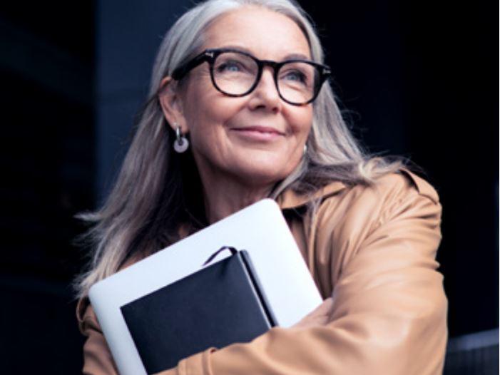 Abbildung einer lächelnden, älteren Frau mit Brille und einem Laptop.