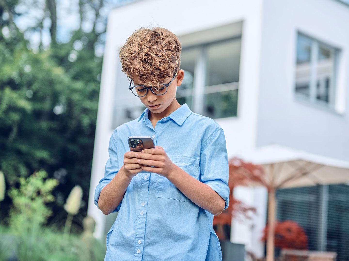 Ein kleiner Junge schaut draußen auf sein Smartphone.