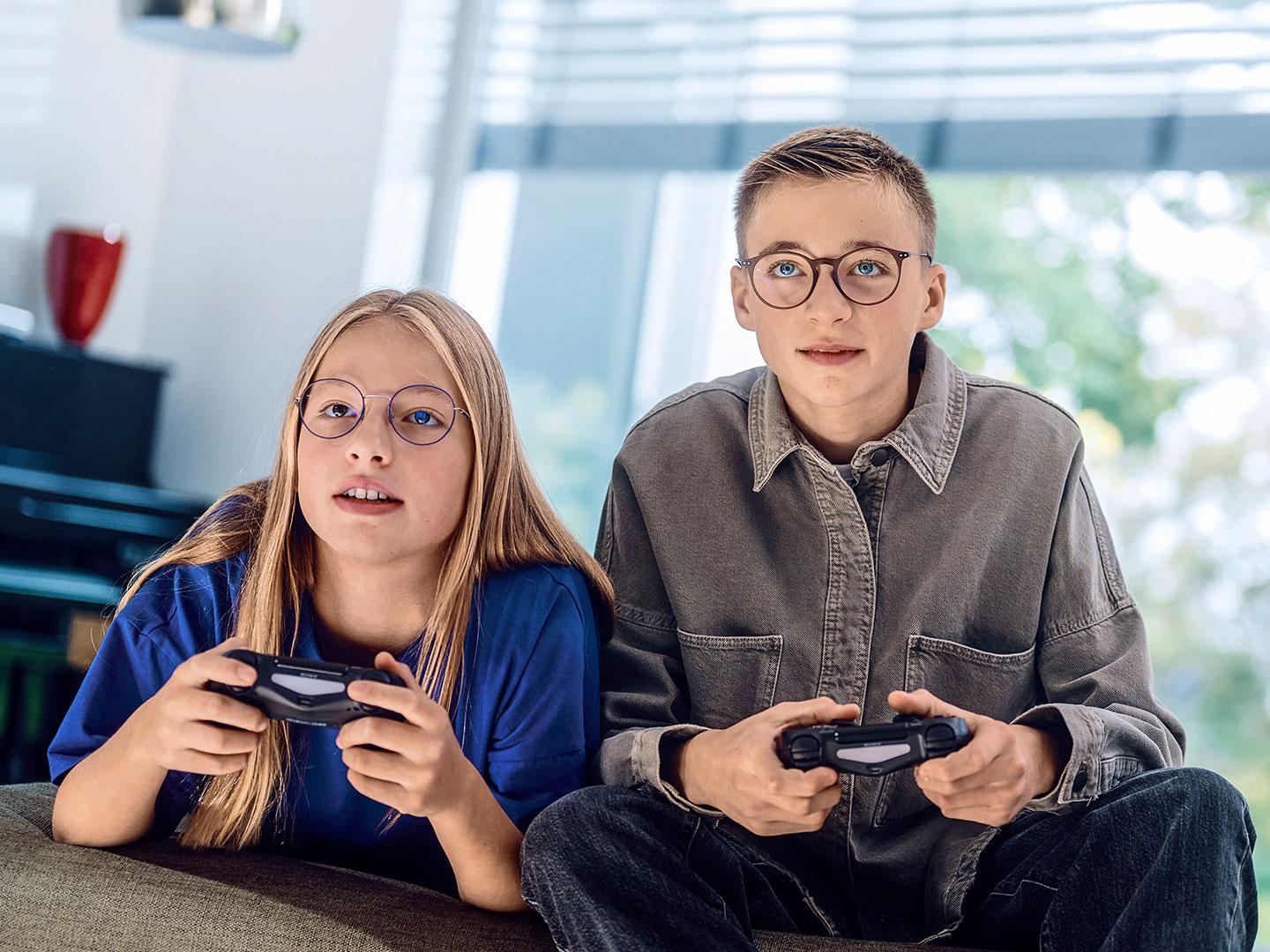 Ein Mädchen und ein Junge im Teenageralter spielen Videospiele auf ihren Spielkonsolen.
