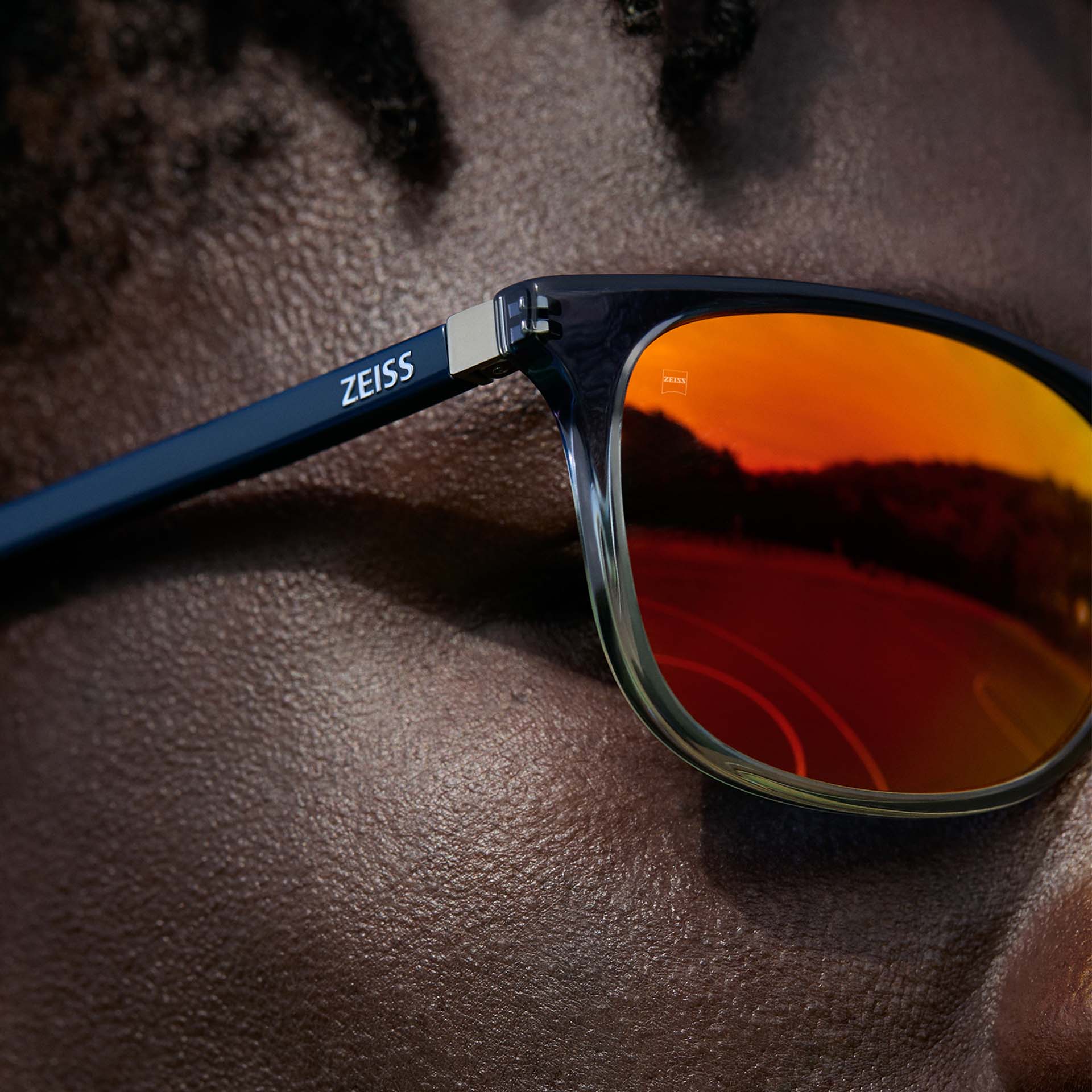 Nahaufnahme eines Mannes, der eine ZEISS Brille trägt, mit ZEISS DuraVision Mirror UV Sonnenbrillenglasbeschichtung in orangener Farbe.