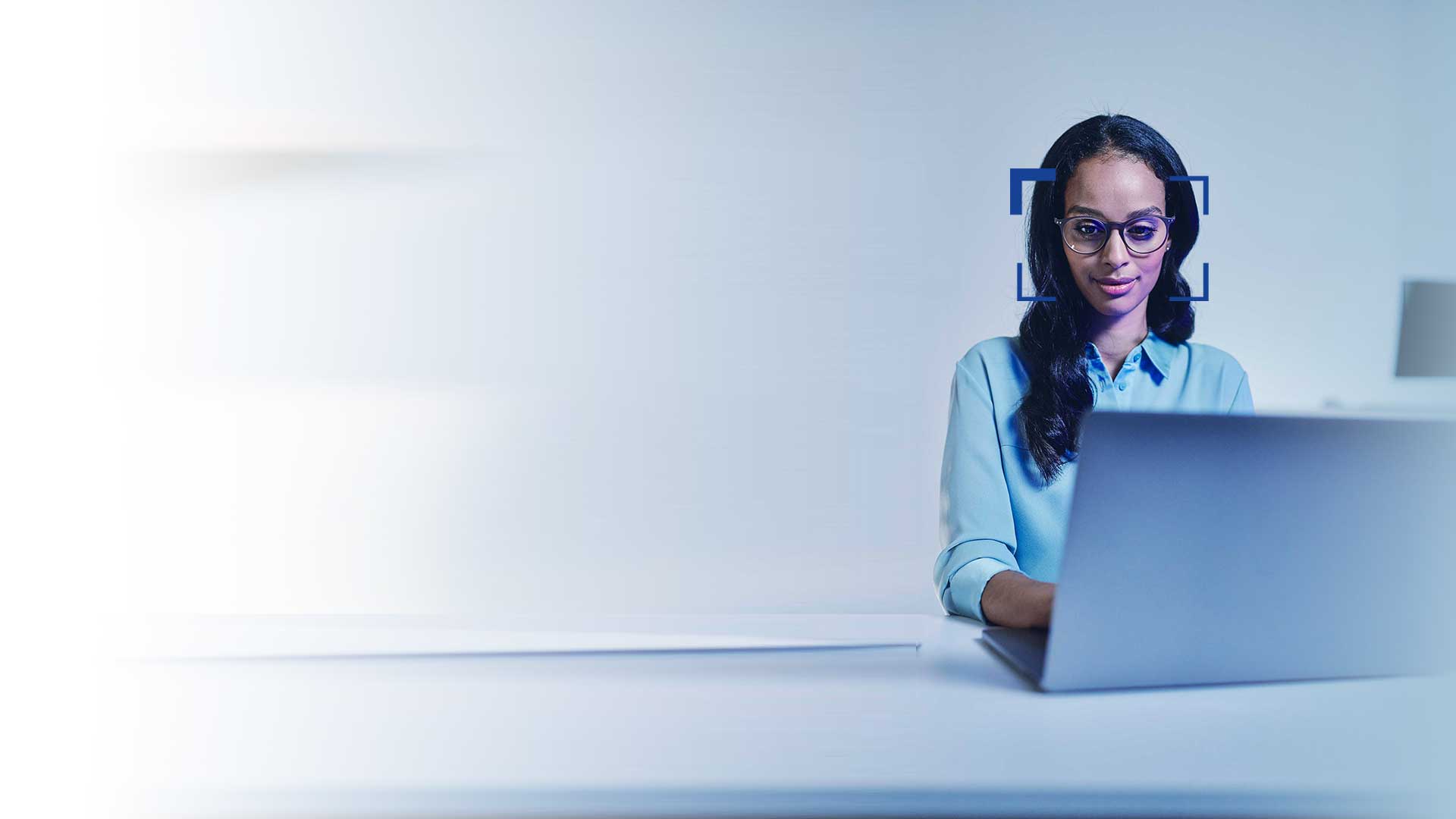 Schwarzhaarige Frau mit Brille schaut lächelnd auf einen Laptop