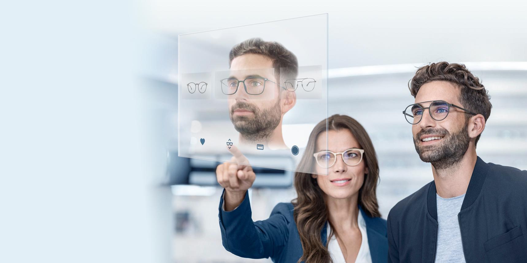 Eine Frau und ein Mann die sich unterschiedliche Brillenmodelle für den Mann auf einem virtuellen Bildschirm ansehen.