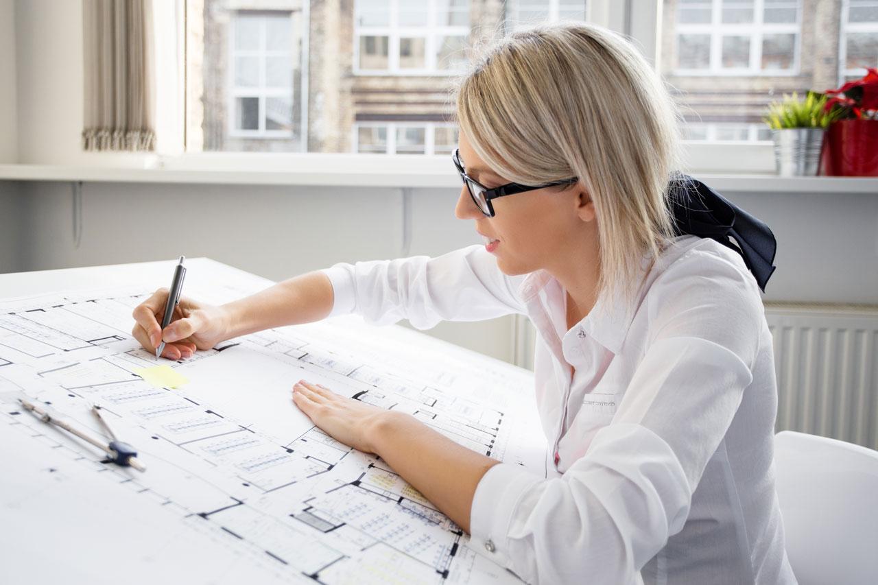 Eine junge Architektin mit Brille arbeitet an einem Bauplan
