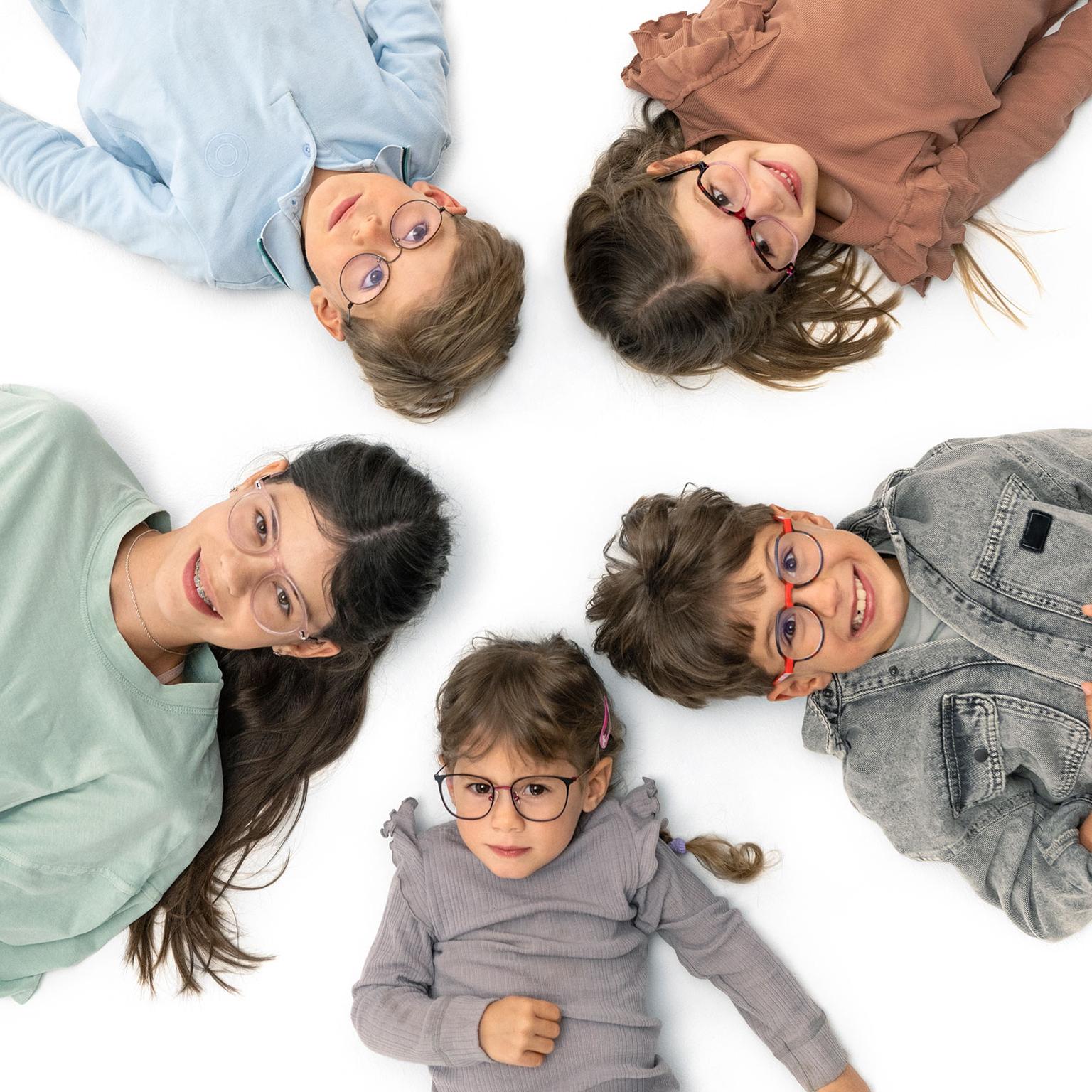 Eine Gruppe von Kindern mit Brille liegt glücklich im Kreis auf dem Boden