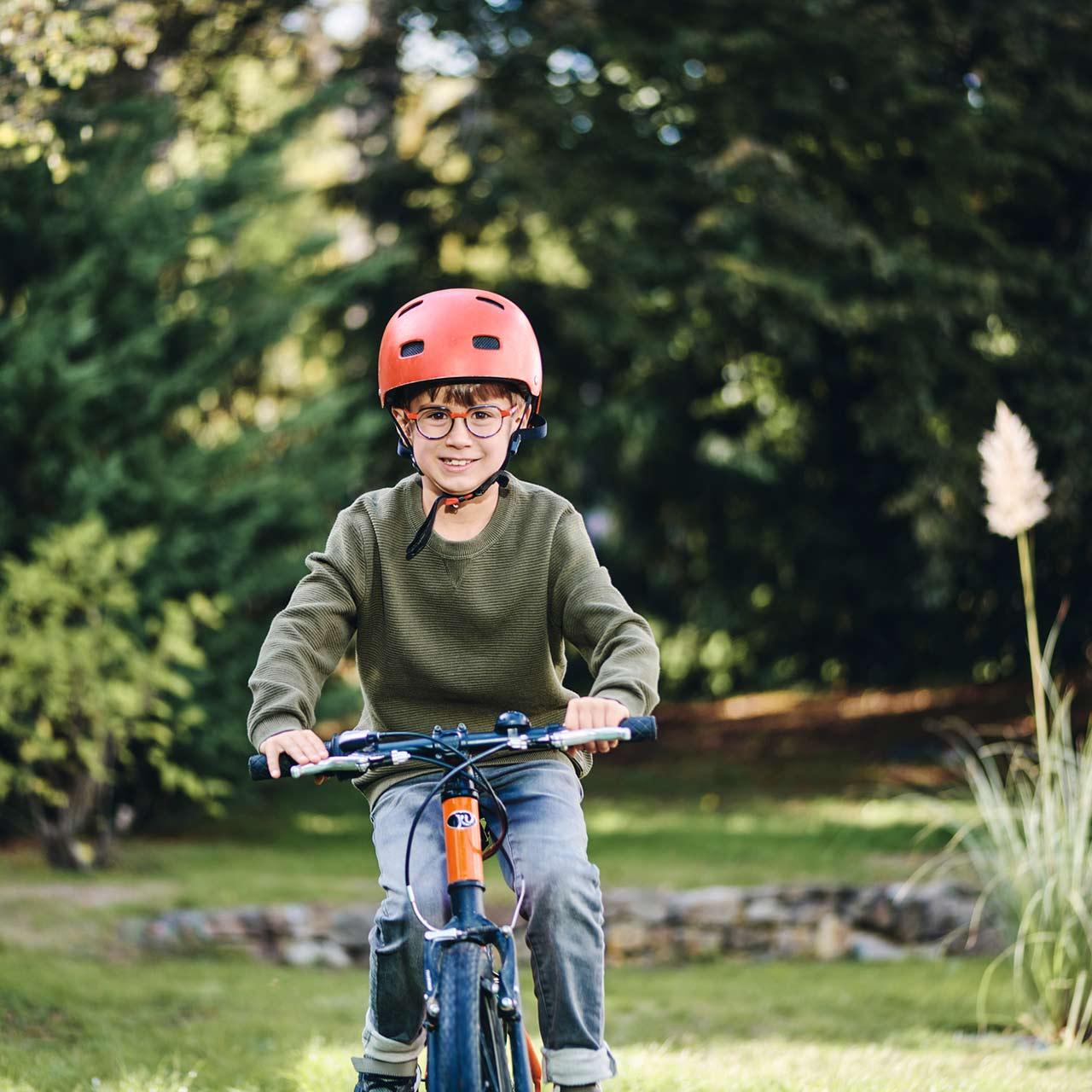 Junge mit Brille fährt lächelnd draußen Fahrrad
