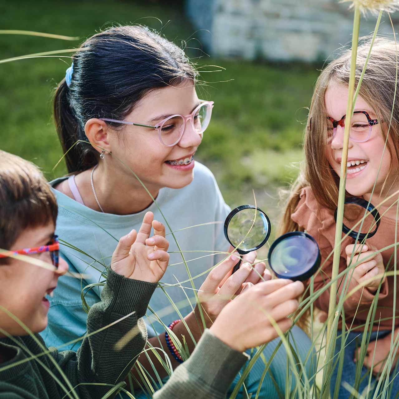 Gruppe von Kindern mit Brille und Lupe, die draußen spielen und lachen 