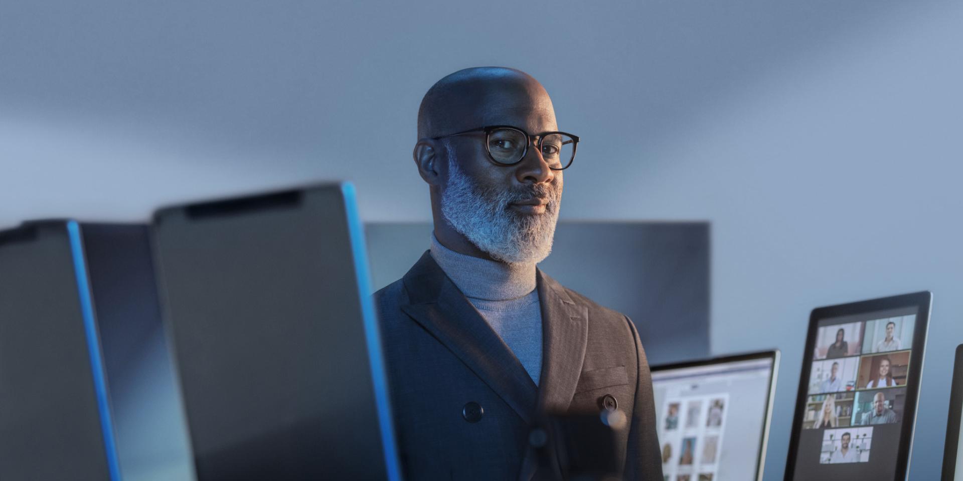 Ein lächelnder, von digitalen Geräten umgebener Mann, trägt zum Schutz vor blauem Licht eine BlueGuard Brille von ZEISS.