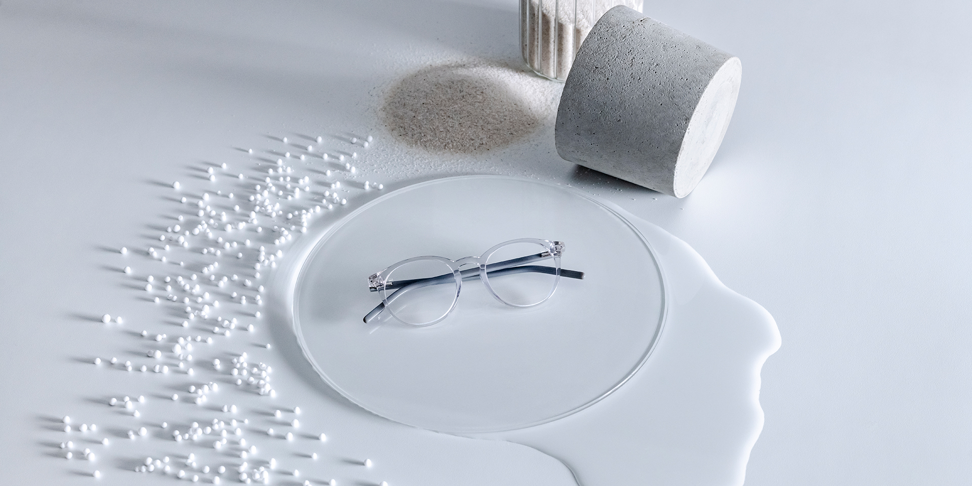 ZEISS Brillengläser mit DuraVision® Beschichtung auf einem Glaspodest, umgeben von Wasser, Sand, Perlen und Steinen.