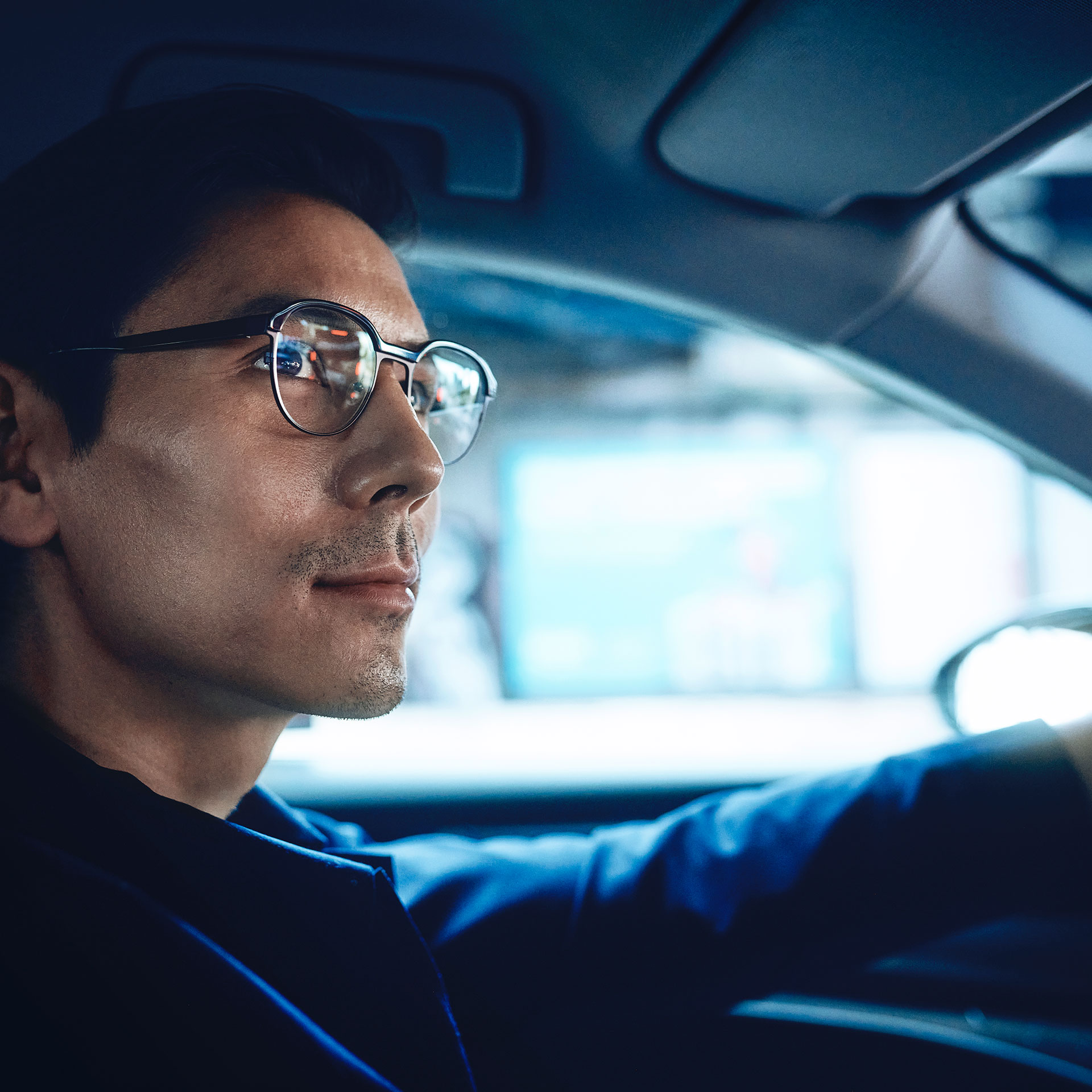 Ein selbstbewusst aussehender Mann fährt Auto und blickt mit einem leichten Lächeln auf die Straße. Er trägt ZEISS DriveSafe Einstärkenbrillengläser.