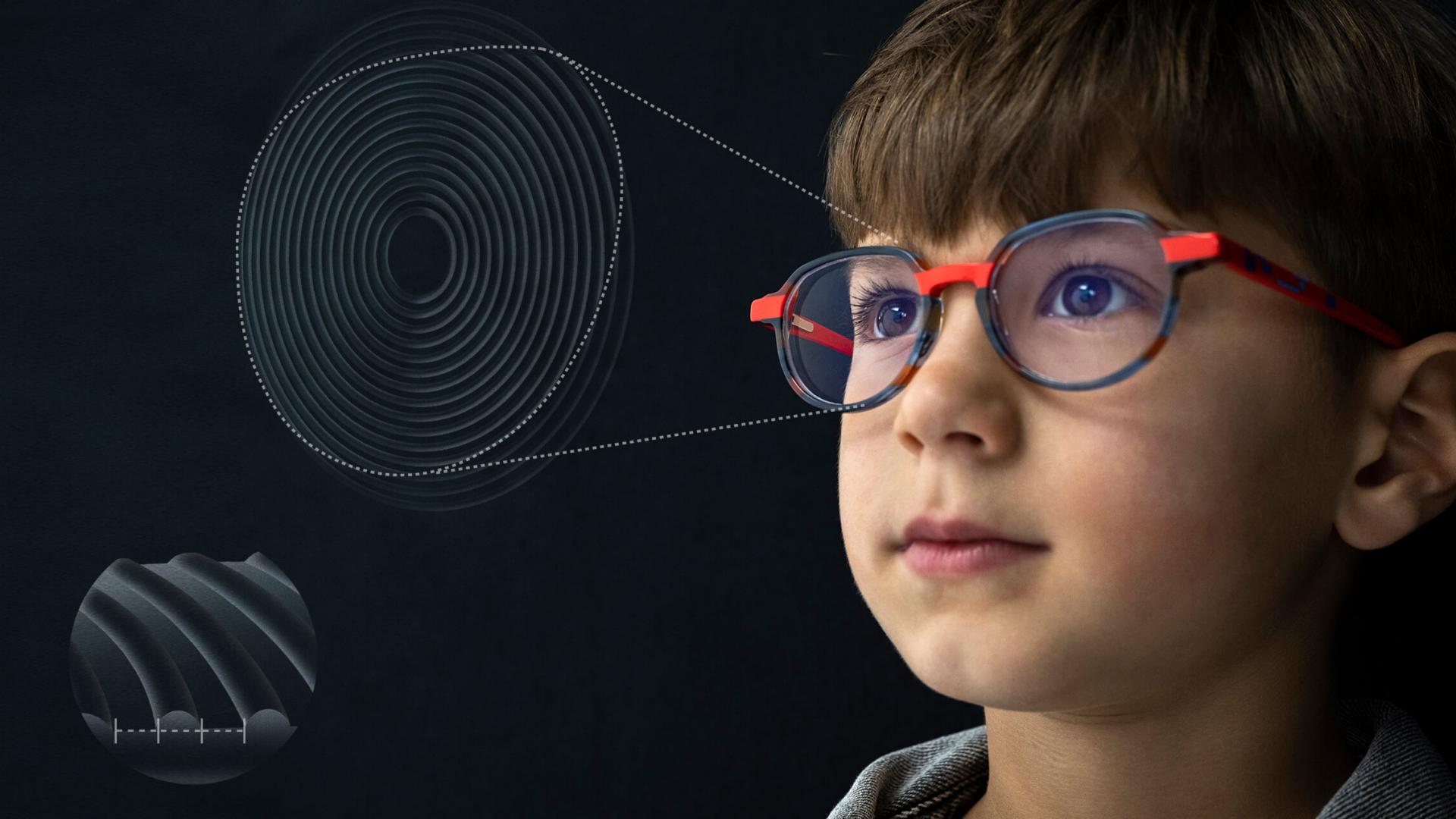 Mann mit Laptop kontrolliert die Brille eines kleinen Jungen. Eine blonde Frau steht hinter dem Kind.