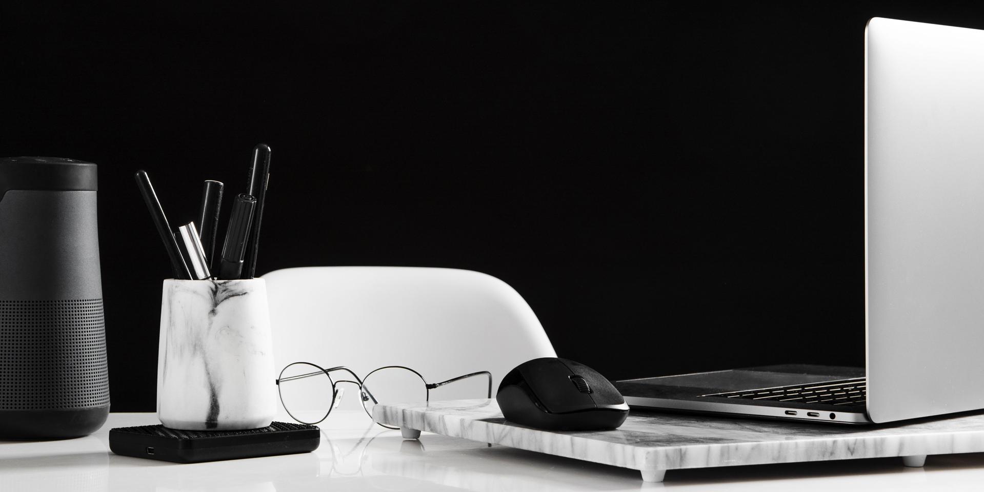 Ein aufgeräumter Arbeitsbereich mit einem geöffneten Laptop auf der rechten Seite und einer Computer-Maus. Davor liegt eine Brille. Auf der linken Seite des Bildes befindet sich ein Behälter mit Stiften.