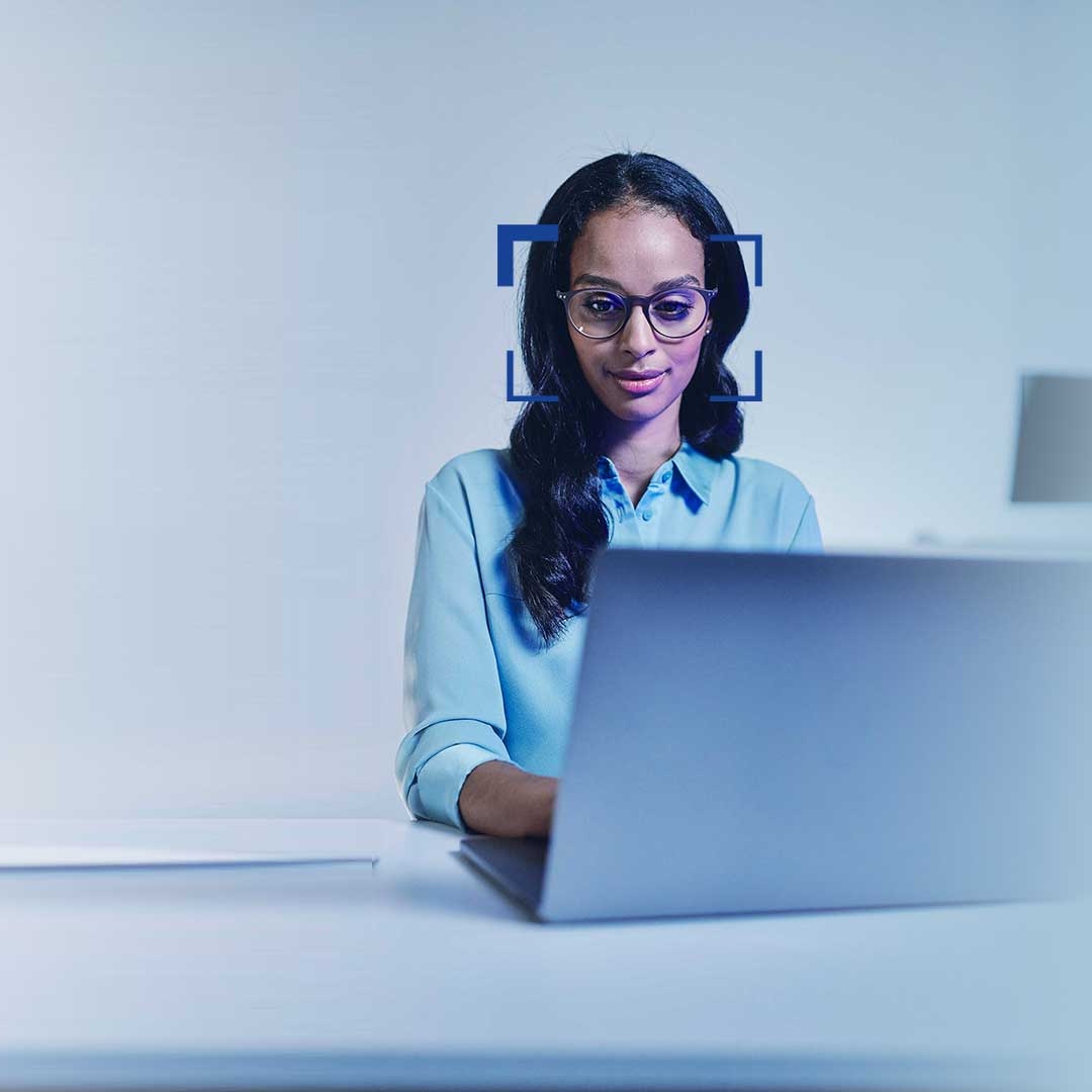 Schwarzhaarige Frau mit Brille schaut lächelnd auf einen Laptop