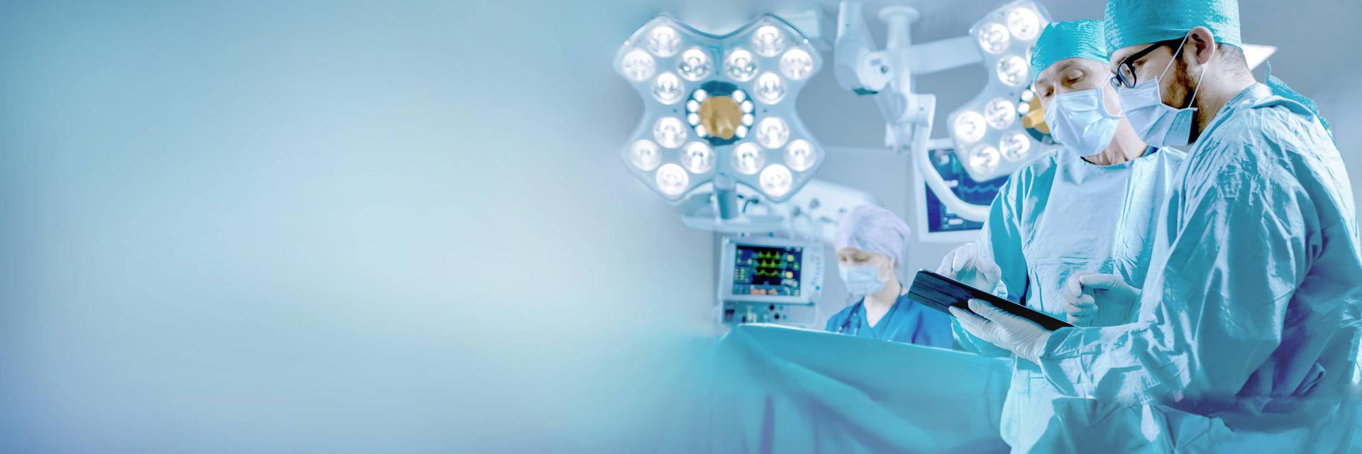 Chirurgen in einem Operationssaal überprüfen unter hellen chirurgischen Lampen Informationen auf einem Tablet, wobei medizinische Geräte von ZEISS sichtbar sind.