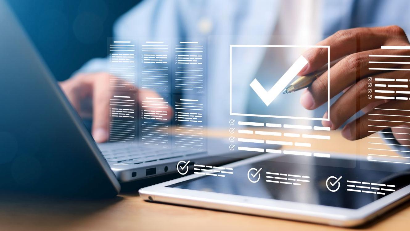 Person using a laptop and tablet with digital checkmarks and data overlays, symbolizing modern technology and quality assurance at ZEISS.
