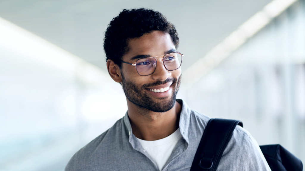 Ein lächelnder junger Mann mit einem Rucksack über der Schulter trägt eine ZEISS SmartLife Digital Brille und schaut zur Seite.